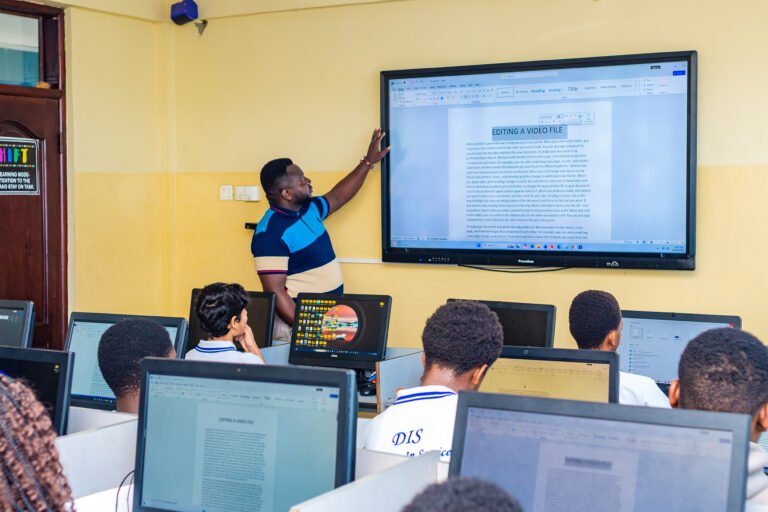 Teacher at the SMART board in the computer lab, with learners at computers